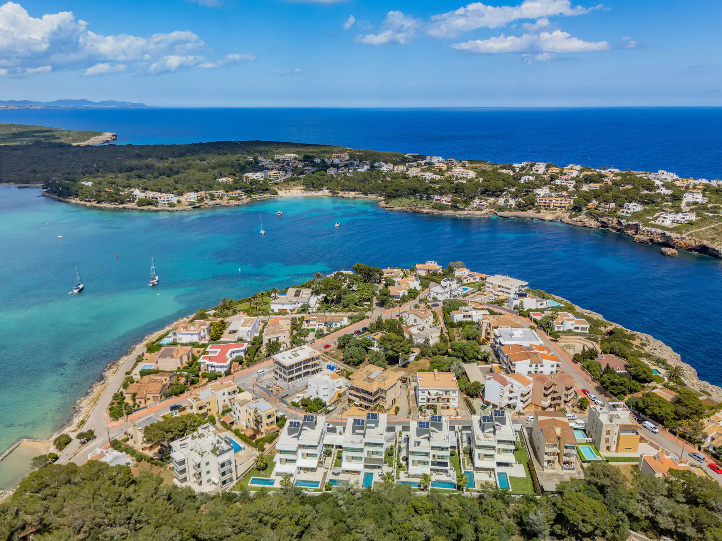 Aerial view of coastal real estate with turquoise water, boats, and white buildings under a blue sky.