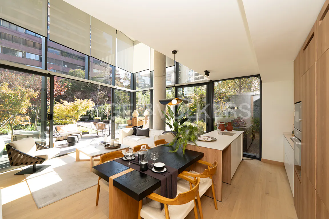 Bright, modern living space with floor-to-ceiling windows overlooking a lush garden. Dining table, kitchen island, and living area visible.