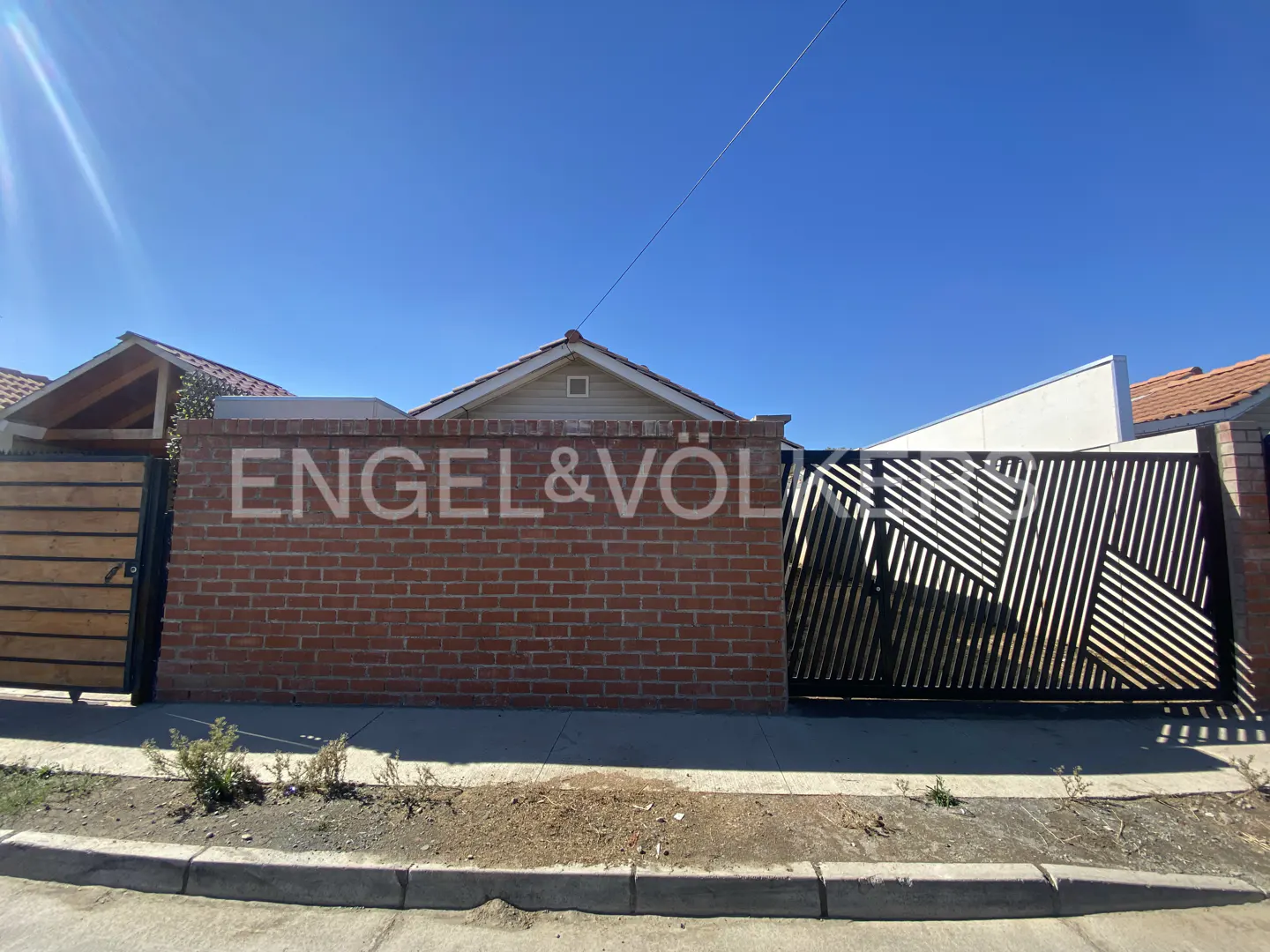 Exterior view of a brick wall with "Engel & Völkers" painted on it, flanked by a wooden gate on the left and a black metal gate on the right.