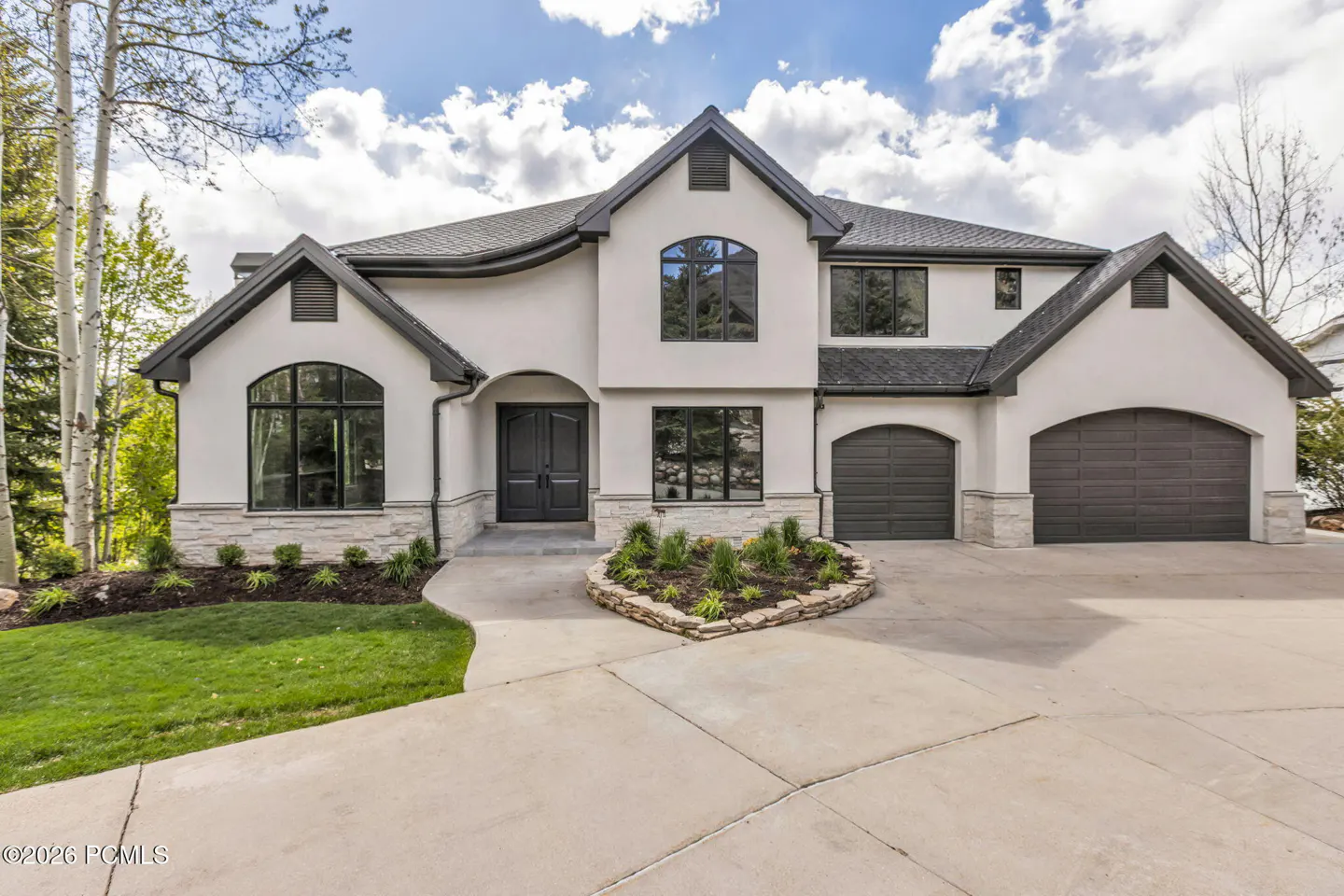 Two-story white stucco house with gray trim, a gray roof, and a concrete driveway on a sunny day.