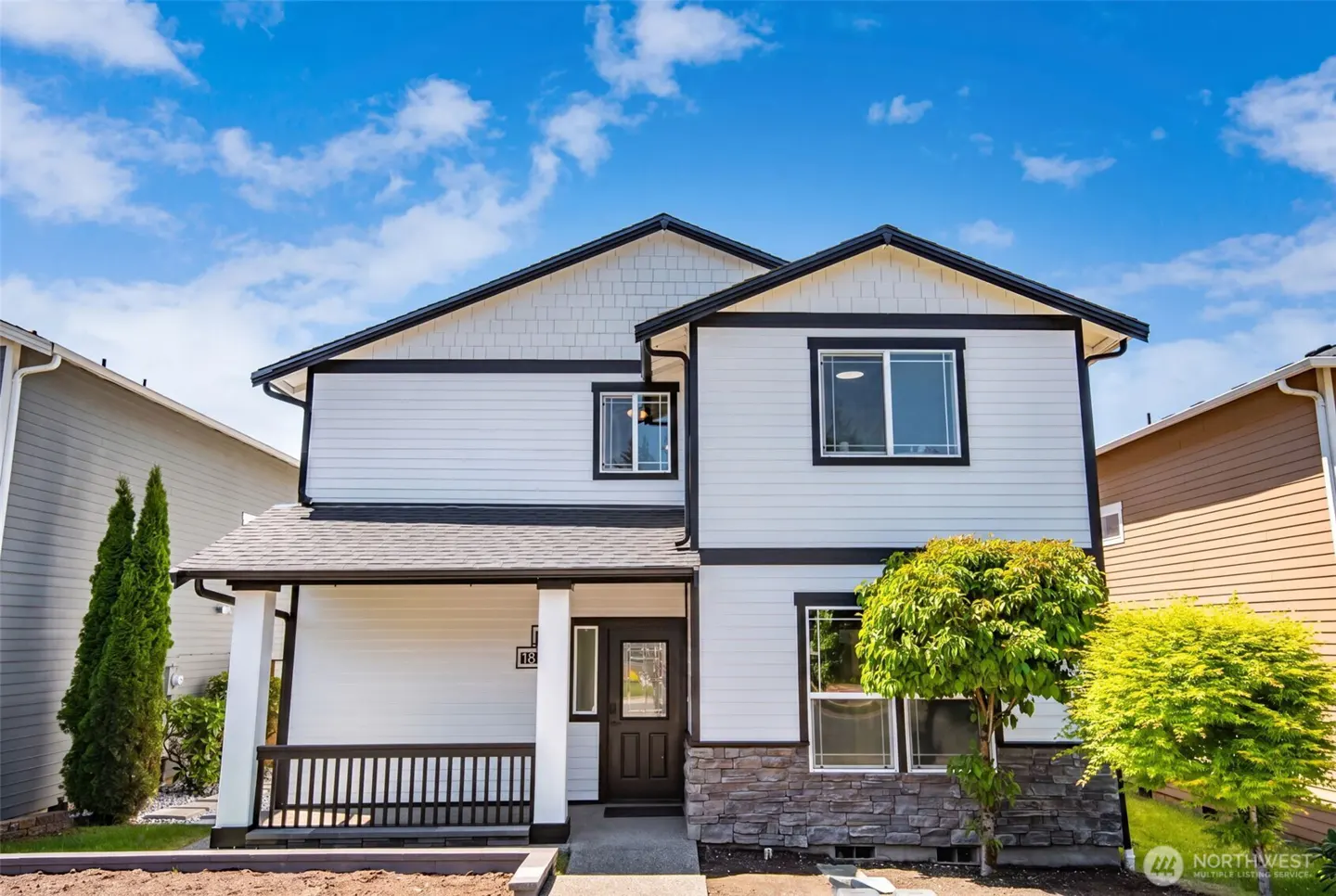 Two-story suburban home with white siding, black trim, a covered front porch, and stone accents under a blue sky.