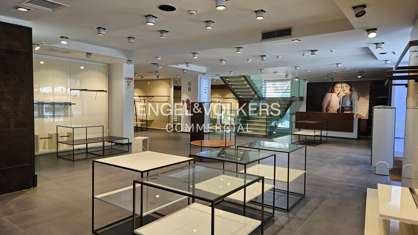 Bright, modern retail space with display tables, gray tile floor, and recessed lighting. Engel & Volkers Commercial logo visible.