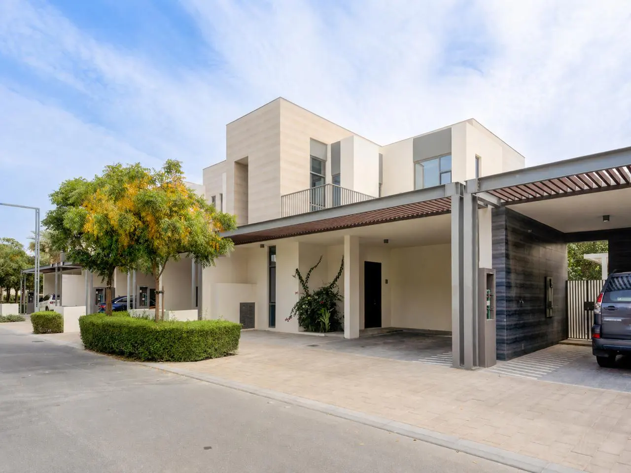Modern two-story home with a carport. The house is light beige with a dark gray carport. A car is parked in the carport.