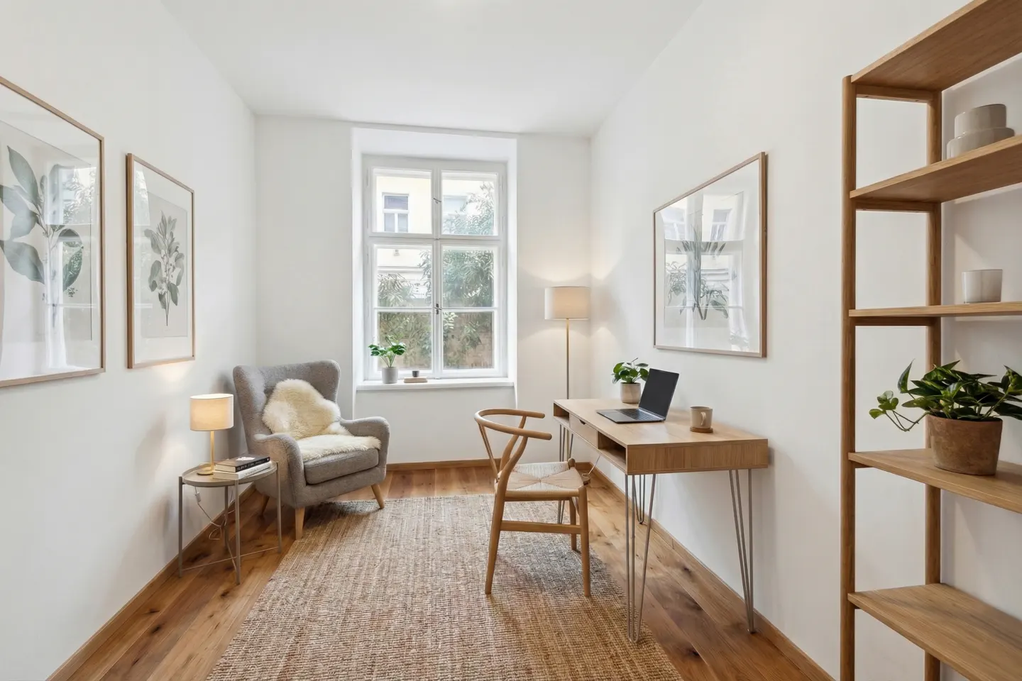 Bright home office with wood floors, a jute rug, and white walls. A gray chair sits near a window, and a wood desk with a laptop faces a bookshelf.