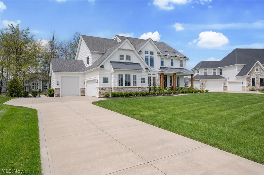 Exterior view of a two-story white house with a gray roof, a large lawn, and a concrete driveway.
