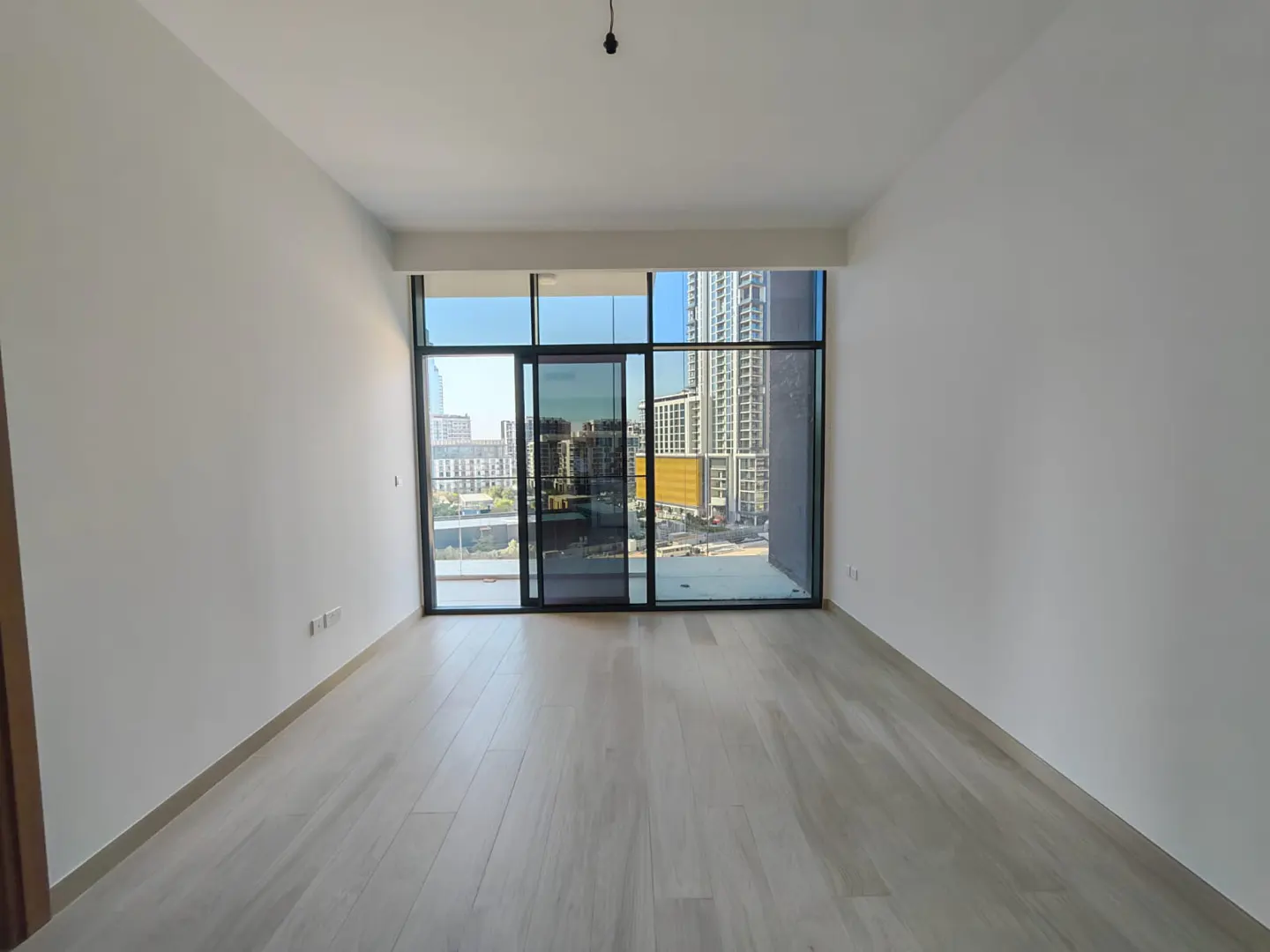 Empty room with white walls and light wood floors. Large sliding glass doors offer a city view.