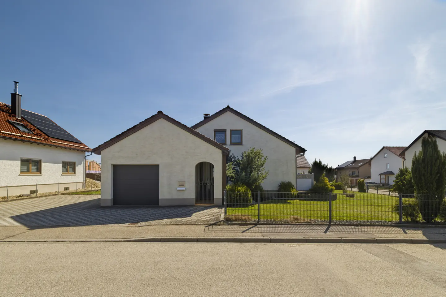 A white house with a gray garage door and a green lawn, under a clear blue sky.