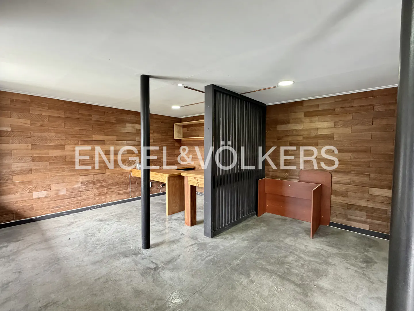 Modern office space with wood-paneled walls, concrete floors, a black slatted room divider, and wooden desks.