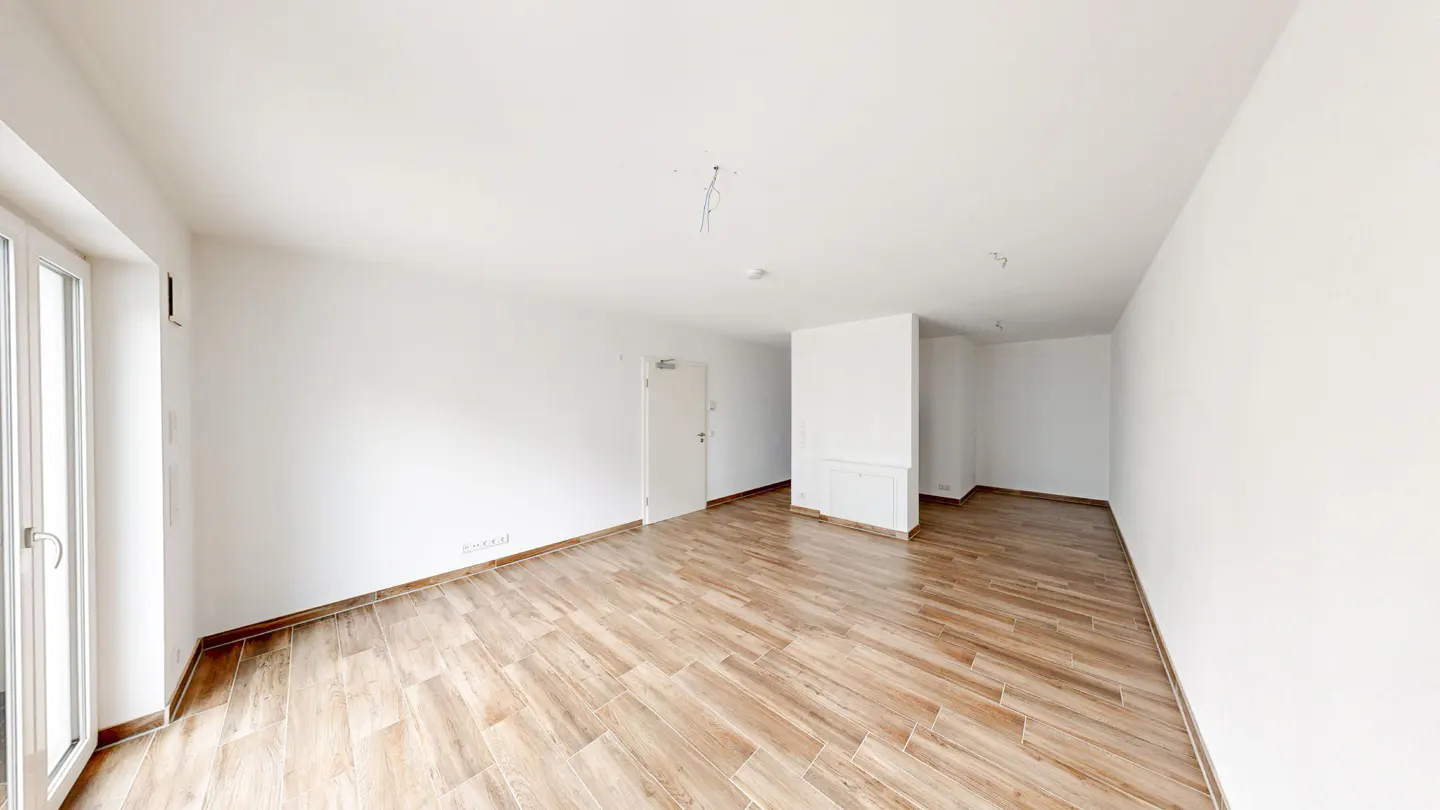 Empty room with white walls, light brown wood-look tile floor, and a white door. A large window is on the left.