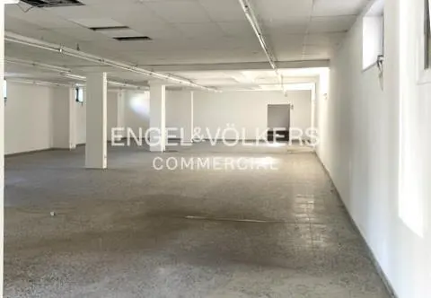 Empty commercial space with white walls, gray concrete floor, and support columns. Engel & Völkers logo in the center.