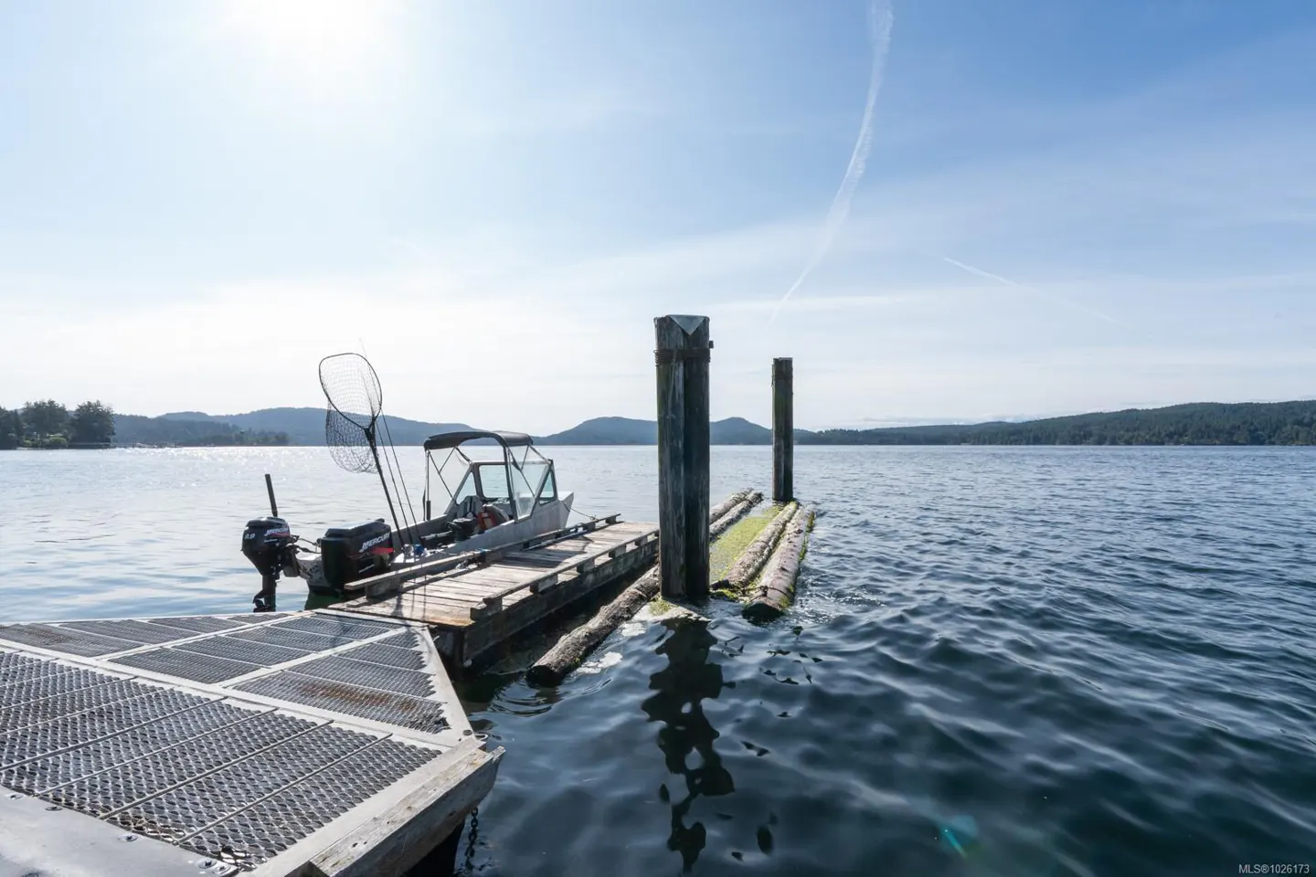 A boat is docked on a wooden pier on a sunny day. The water is calm and blue, and there are mountains in the distance.