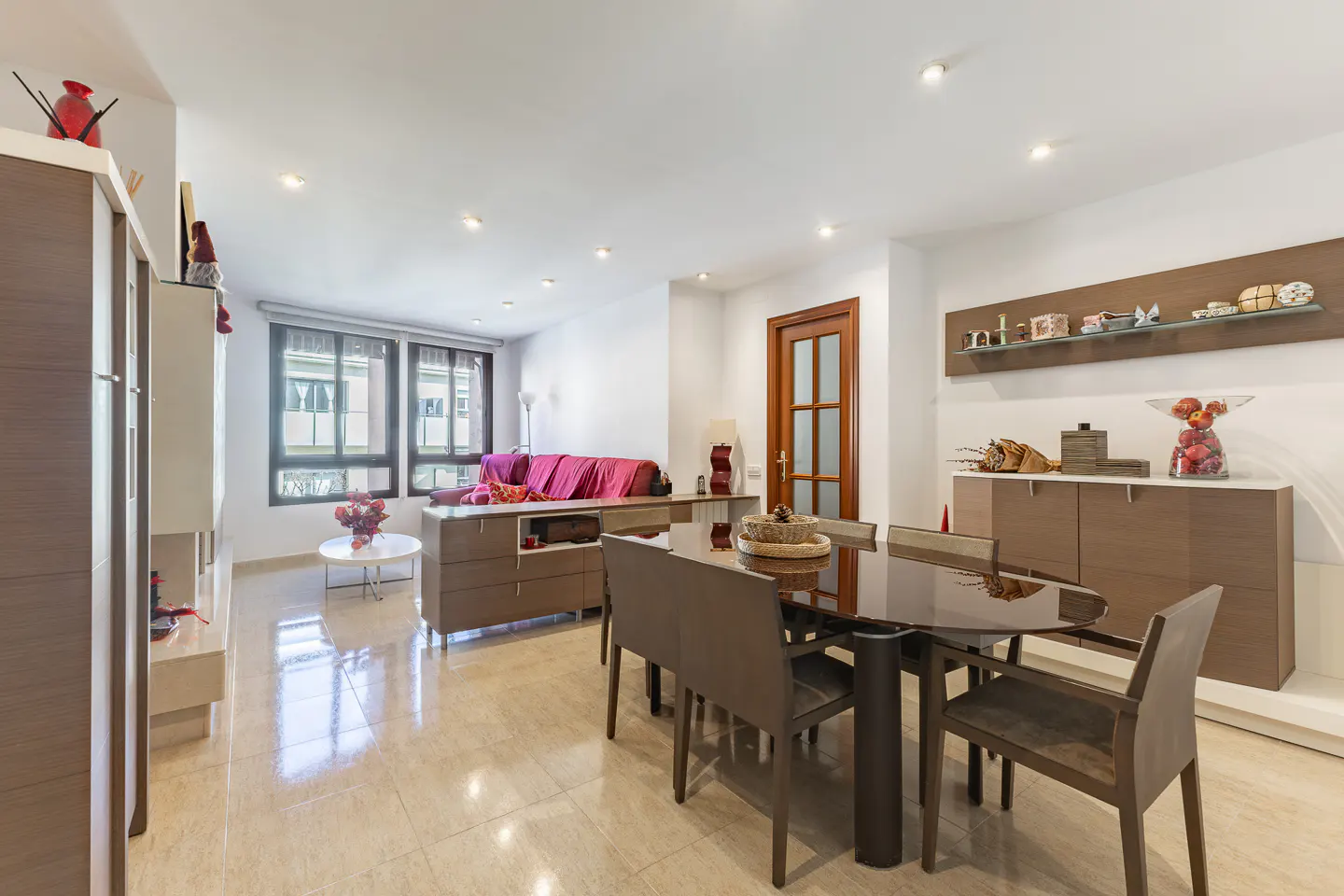 Bright, modern living and dining area with a dark wood table and chairs on a beige tile floor. A pink sofa is visible in the background.
