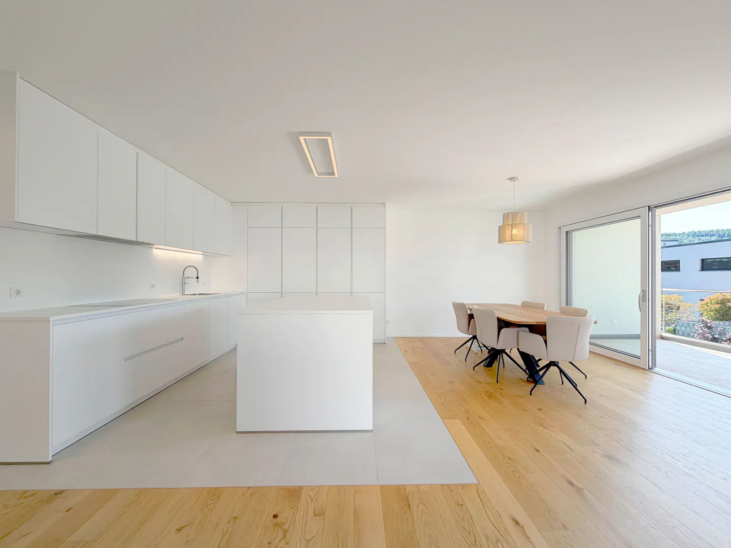 Modern open-plan kitchen with white cabinets, a central island, and a dining area with light wood floors and patio access.