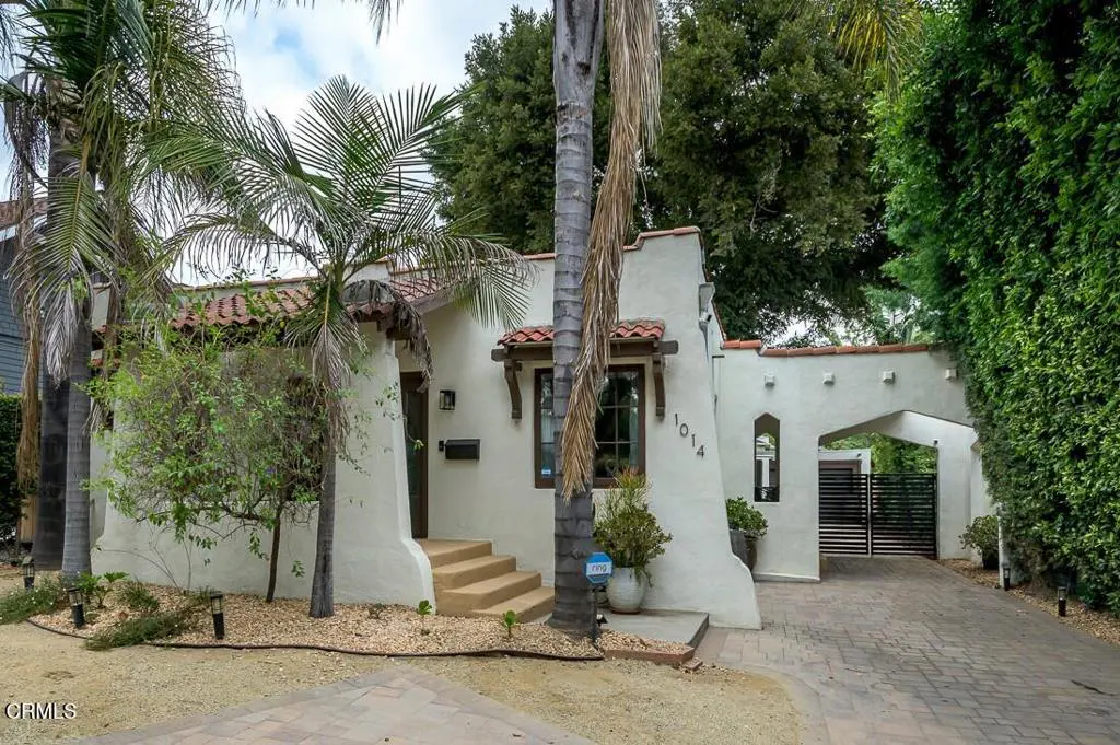 A white stucco house with a red tile roof and palm trees in the front yard. The house number "1014" is visible. A gated driveway is on the right.