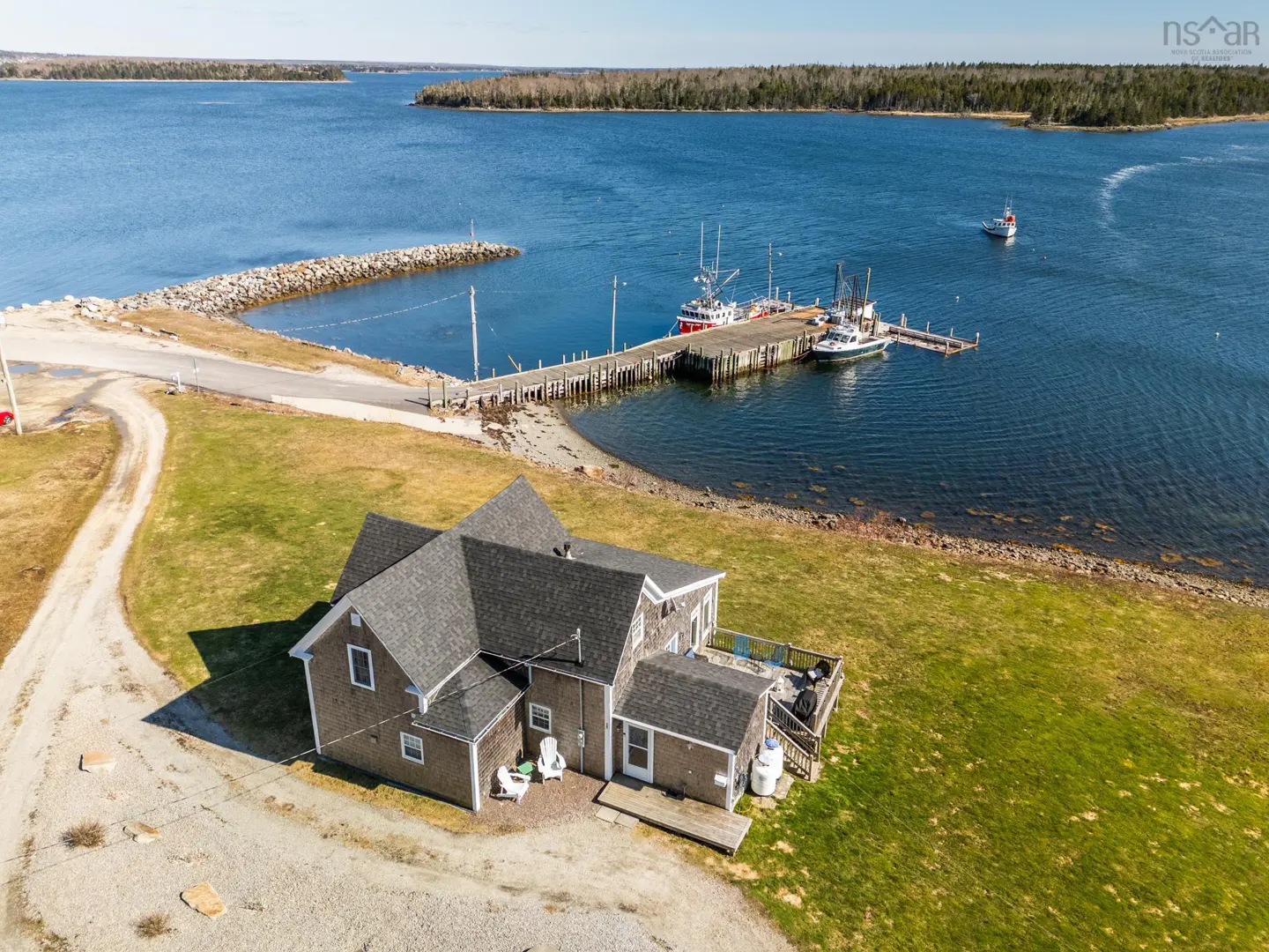 Aerial view of a gray house on a green lawn near a blue bay with a dock and boats.