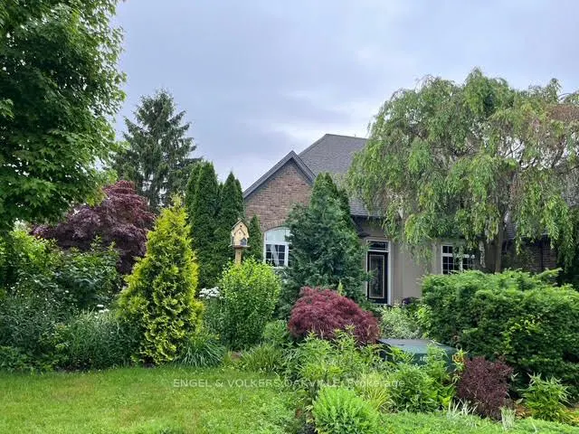 A single-family home with a brick facade and a gray roof, surrounded by lush green landscaping.