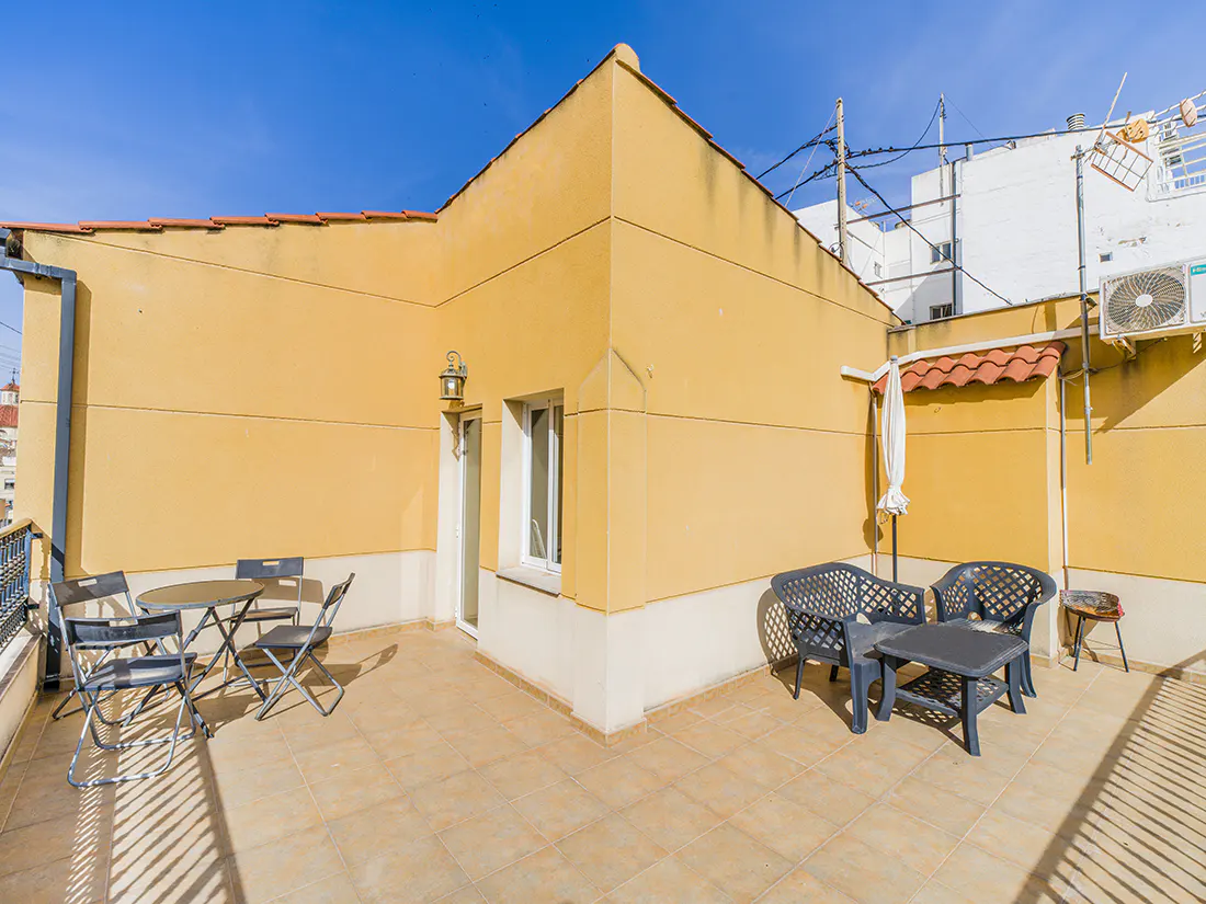 Outdoor patio with yellow walls, tiled floor, and blue sky. There are two seating areas with tables and chairs.