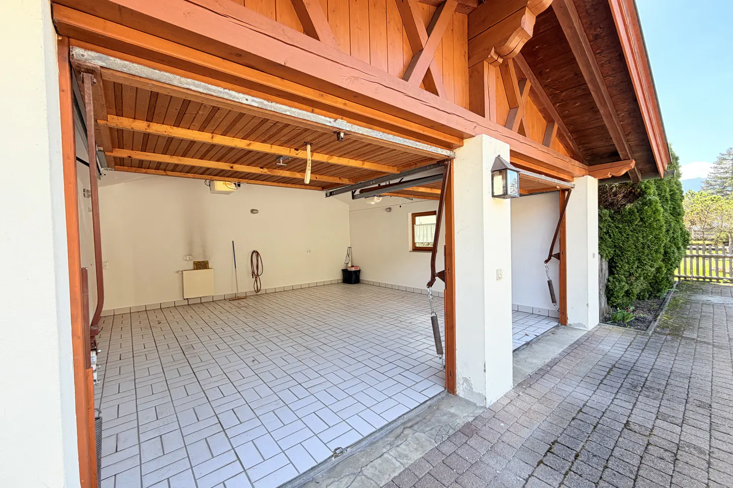 Open garage with white walls, tiled floor, and brown wood trim. A window is visible in the back wall.