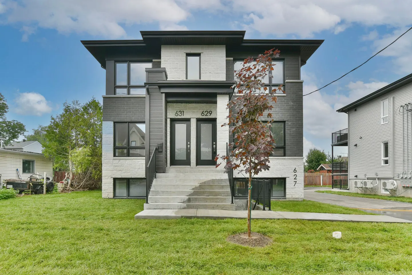 Two-story duplex with gray brick and white stone facade, black trim, and a small tree in the front yard. Addresses 627, 629, and 631 are visible.