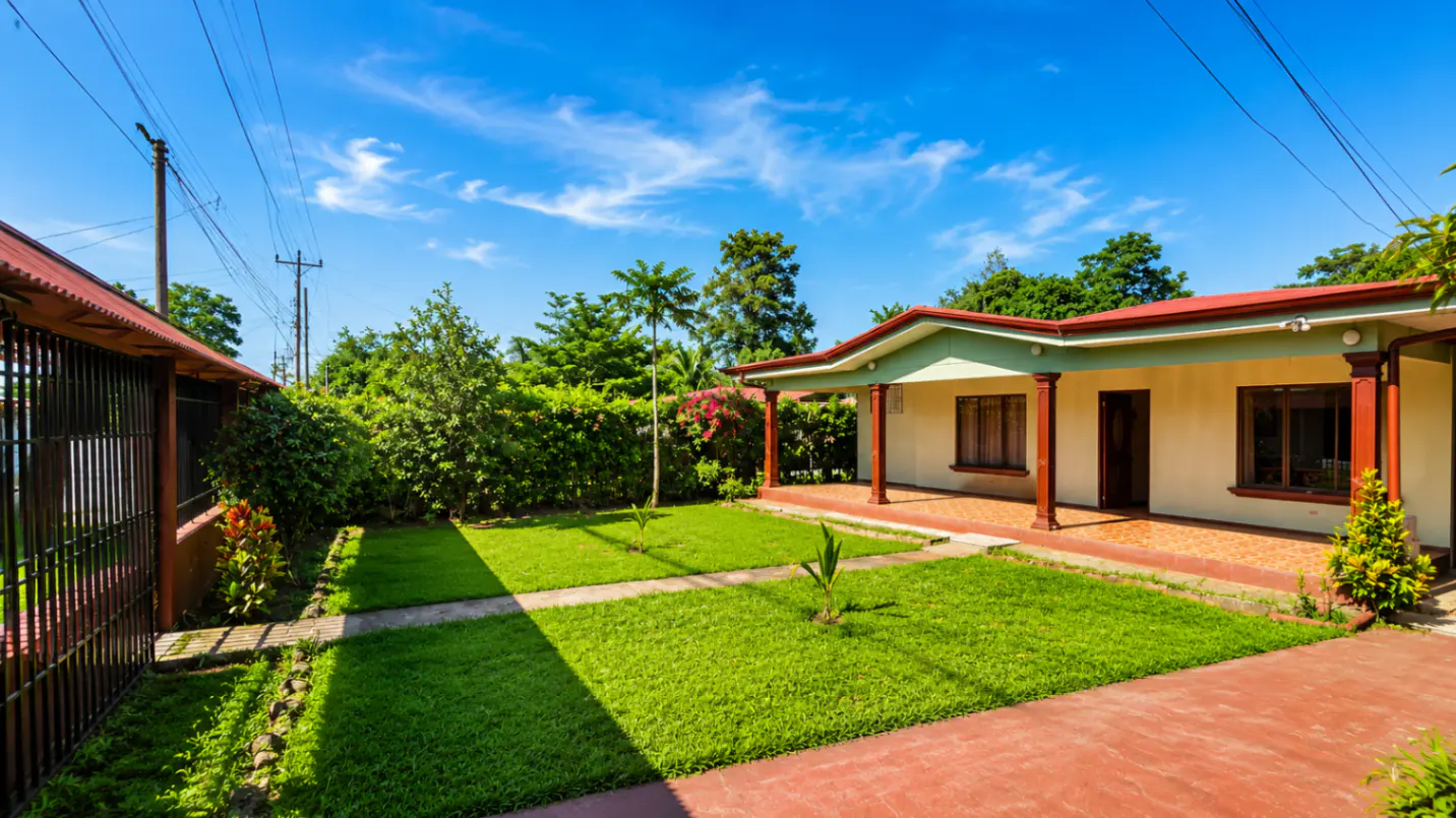 Exterior of a single-story home with a red roof, green trim, and a well-manicured lawn under a bright blue sky.