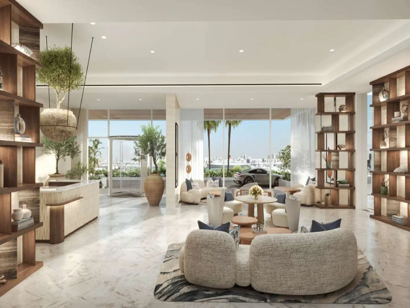 A bright, modern lobby with beige sofas, wooden shelves, and a view of a car and palm trees.