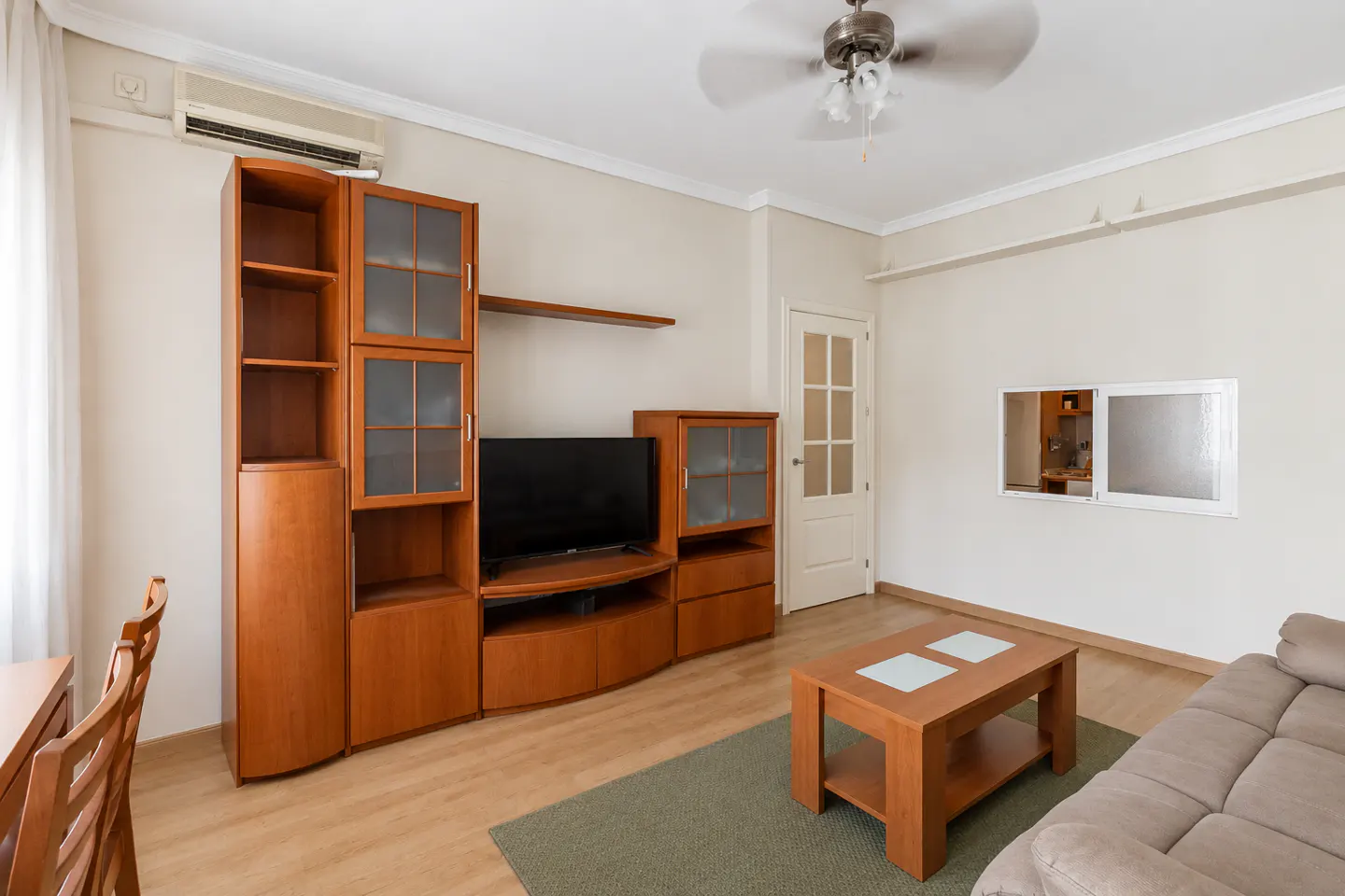 Living room with wood entertainment center, TV, coffee table, and beige sofa on a green rug. A ceiling fan is above.