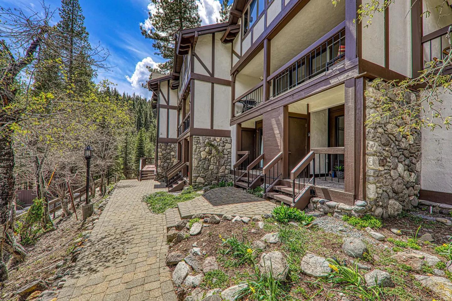 Exterior view of a multi-story condo building with stone accents and brown trim, surrounded by trees and a brick walkway.