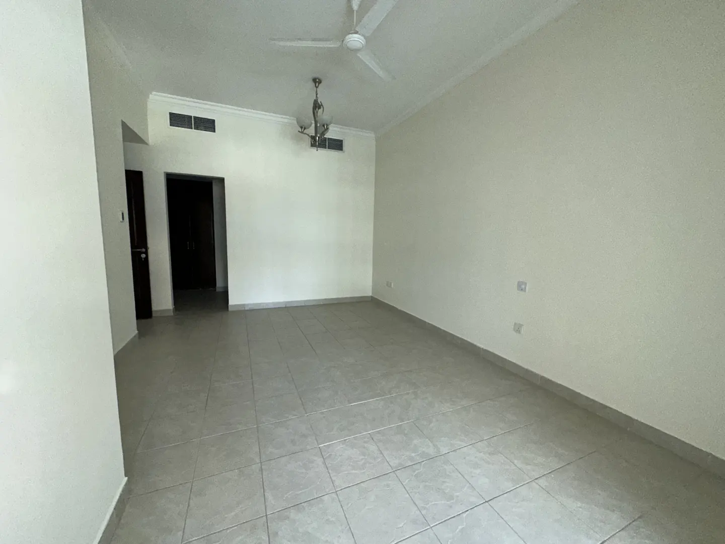 Empty room with light gray tile floor, white walls, ceiling fan, and chandelier. Two dark doorways are visible.