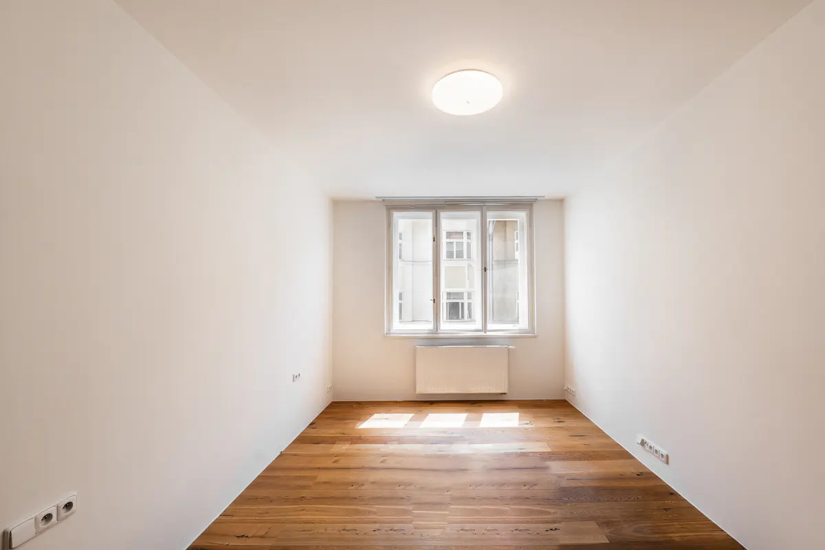 Bright, empty room with hardwood floors, white walls, and a window. A white radiator sits beneath the window.