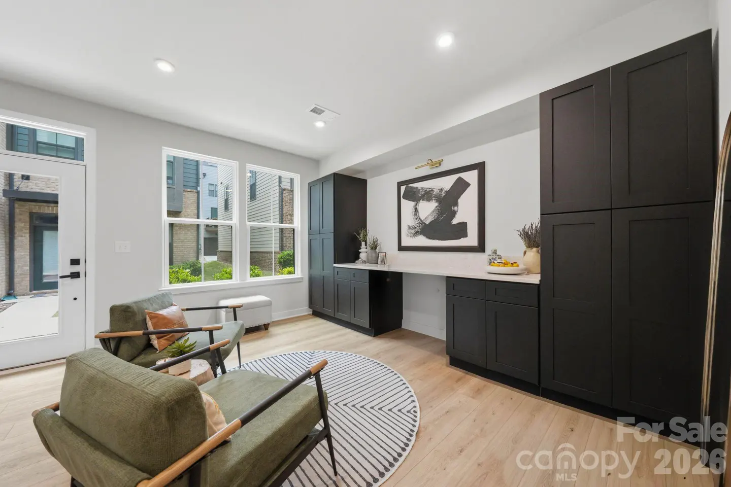A modern living room with two green armchairs, a round rug, and black cabinets with a white countertop. A black and white painting hangs above the counter.