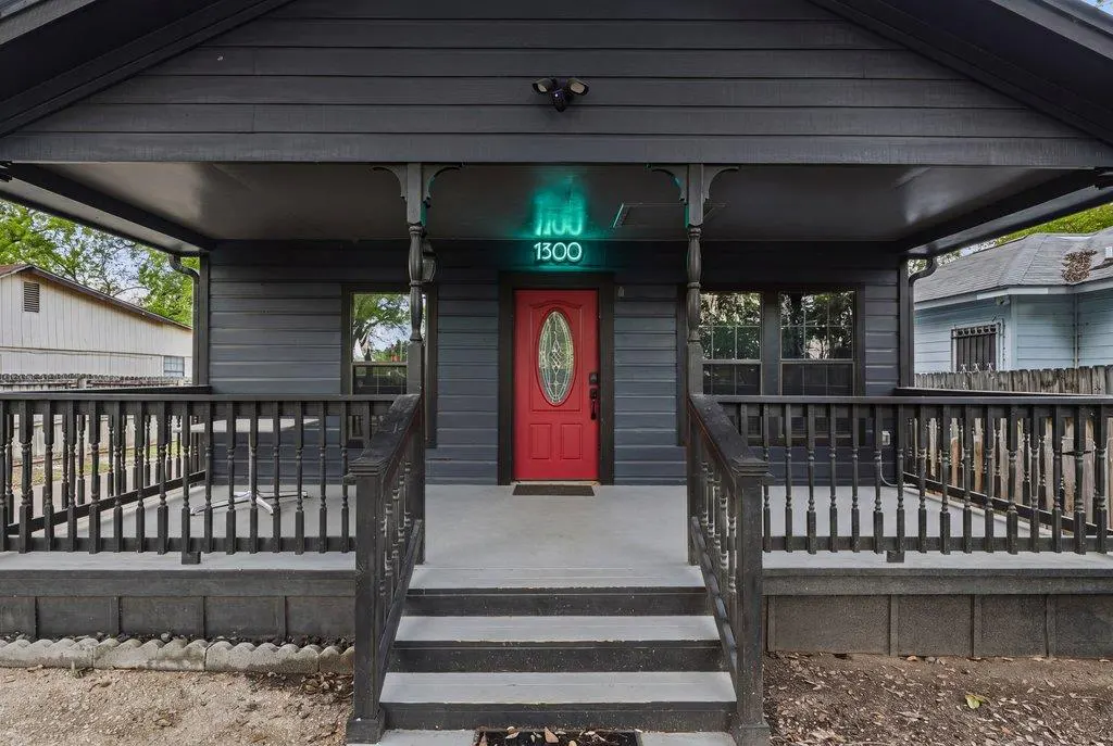 Exterior of a dark gray house with a red front door and a porch with black railings. A bright teal "1300" is above the door.
