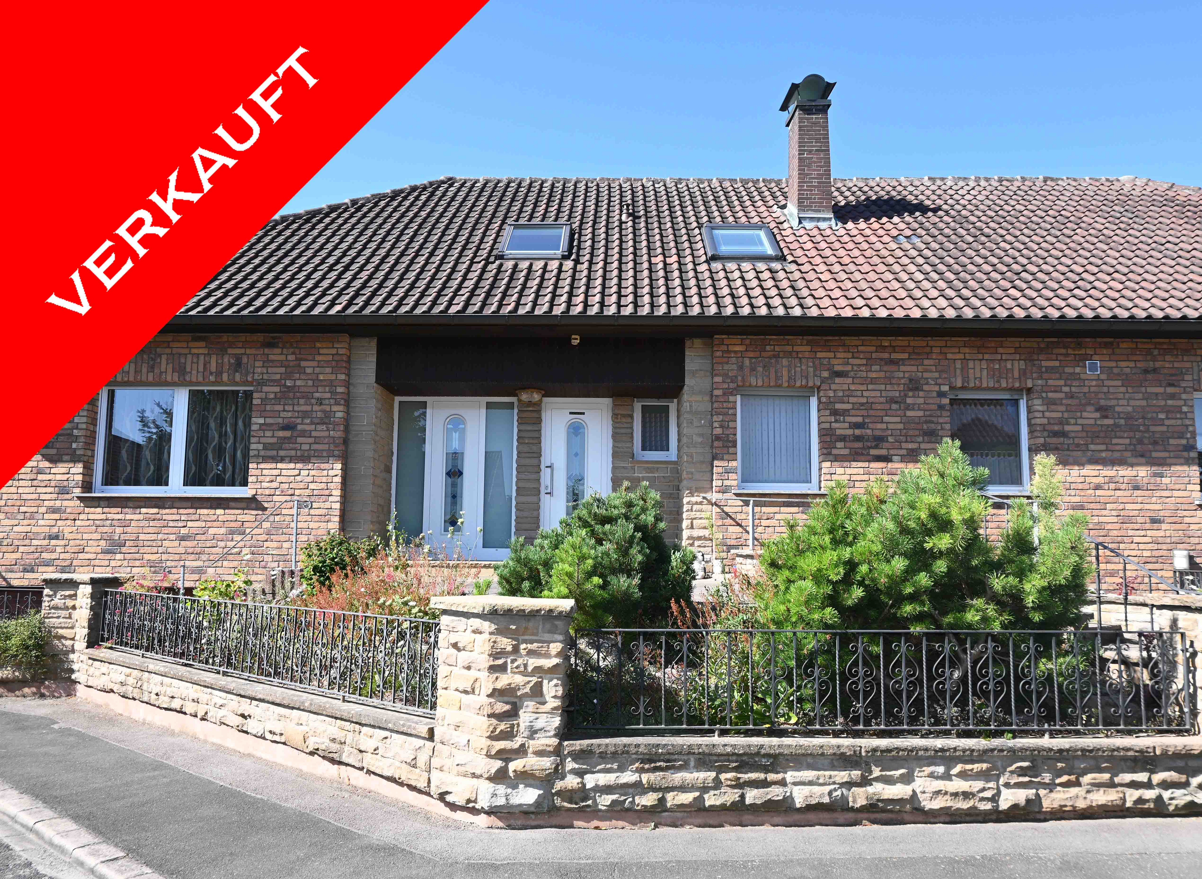 Single-story brick house with a tiled roof, front garden, and a red "SOLD" banner in the corner against a clear blue sky. [AI-generated text]