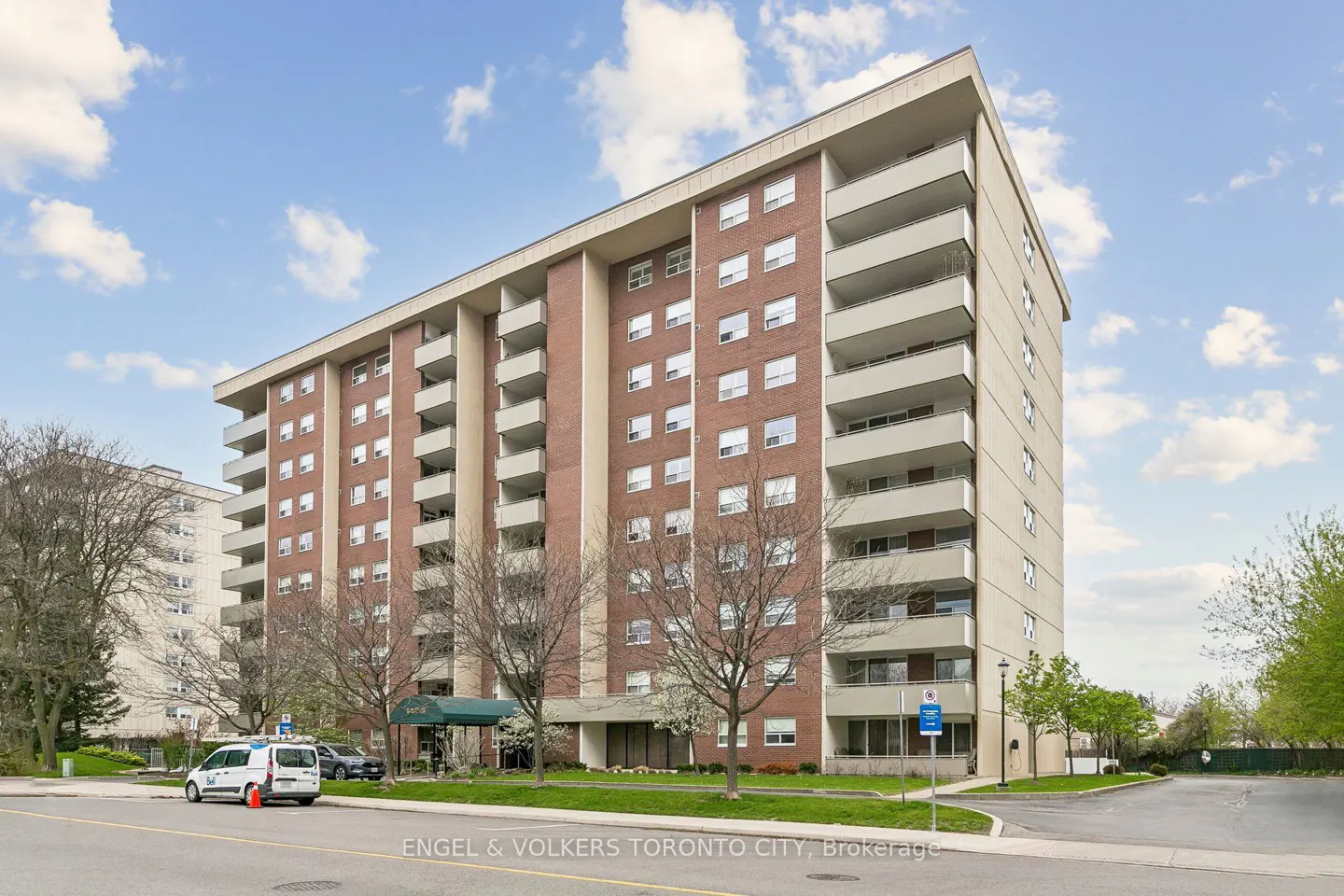 Exterior view of a tall brick apartment building with white balconies under a blue sky with clouds.