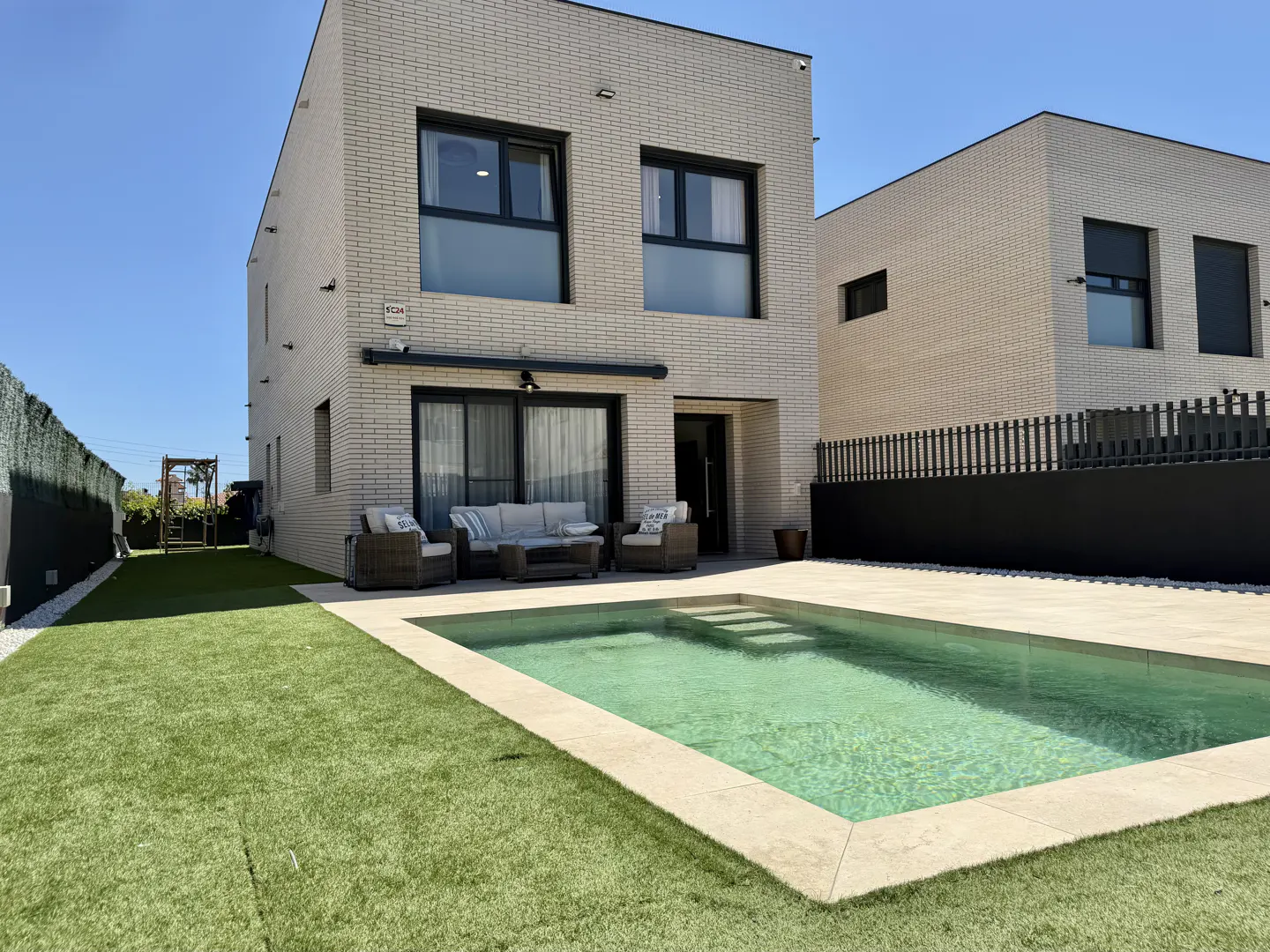 Backyard view of a modern two-story house with a pool, patio furniture, and green grass.