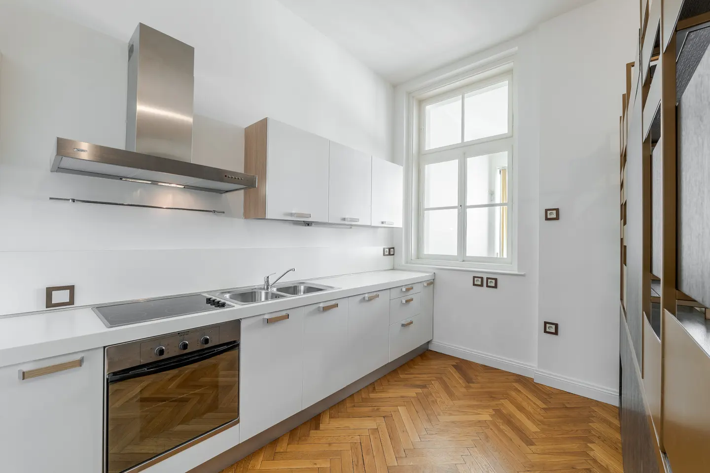 Bright kitchen with white cabinets, stainless steel appliances, and herringbone wood floor. A large window provides natural light.