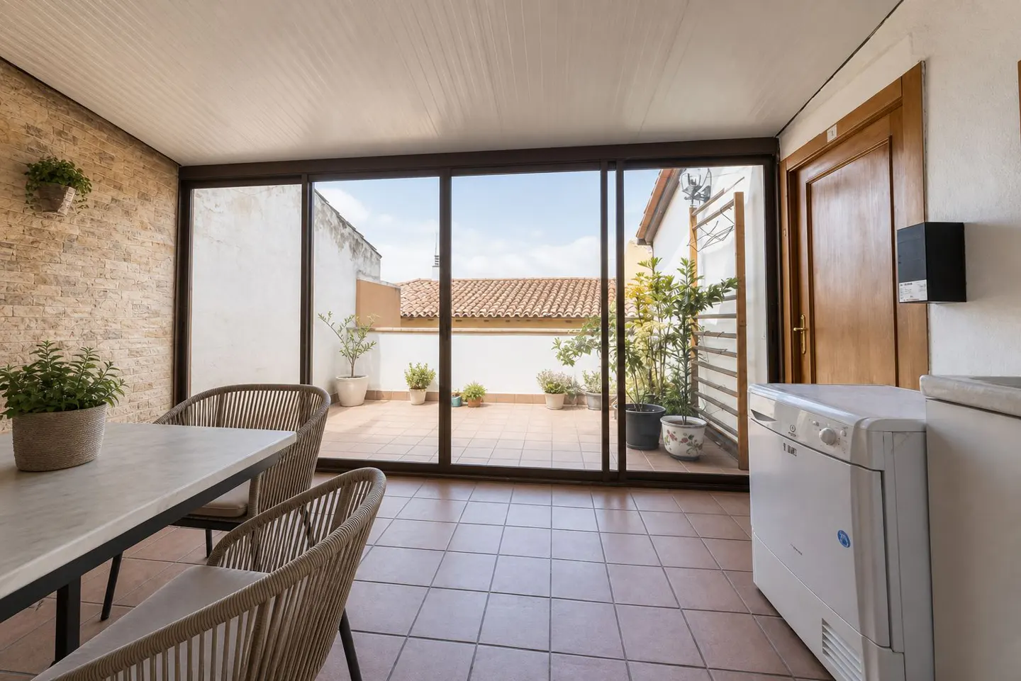Sunroom with a table, chairs, and a view of a rooftop terrace through sliding glass doors. A washing machine is visible on the right.
