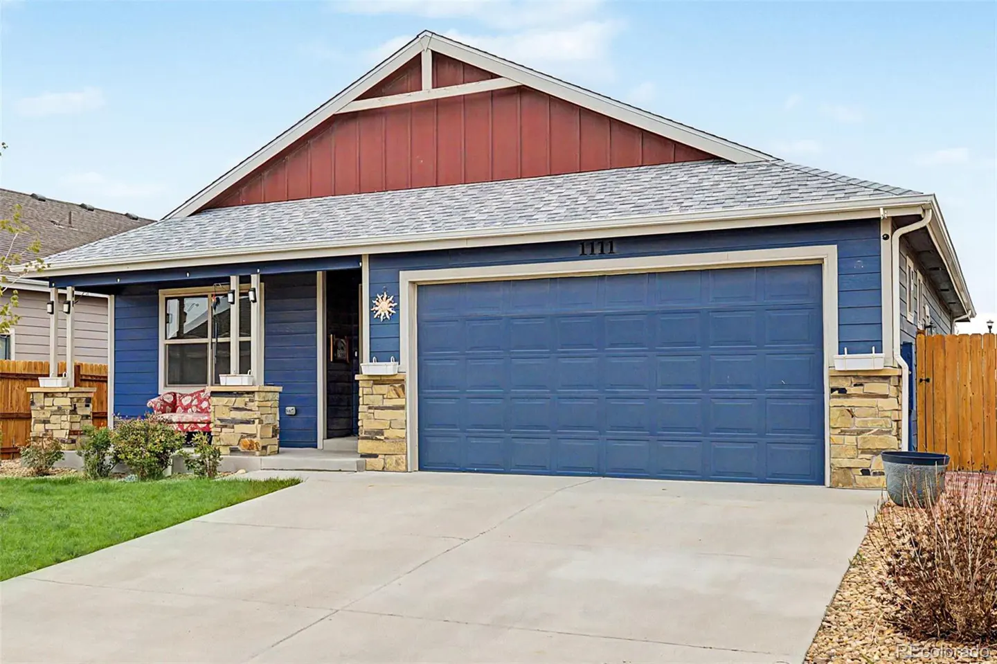 Blue house with a red gable, stone accents, and a large blue garage door. A concrete driveway leads to the house.