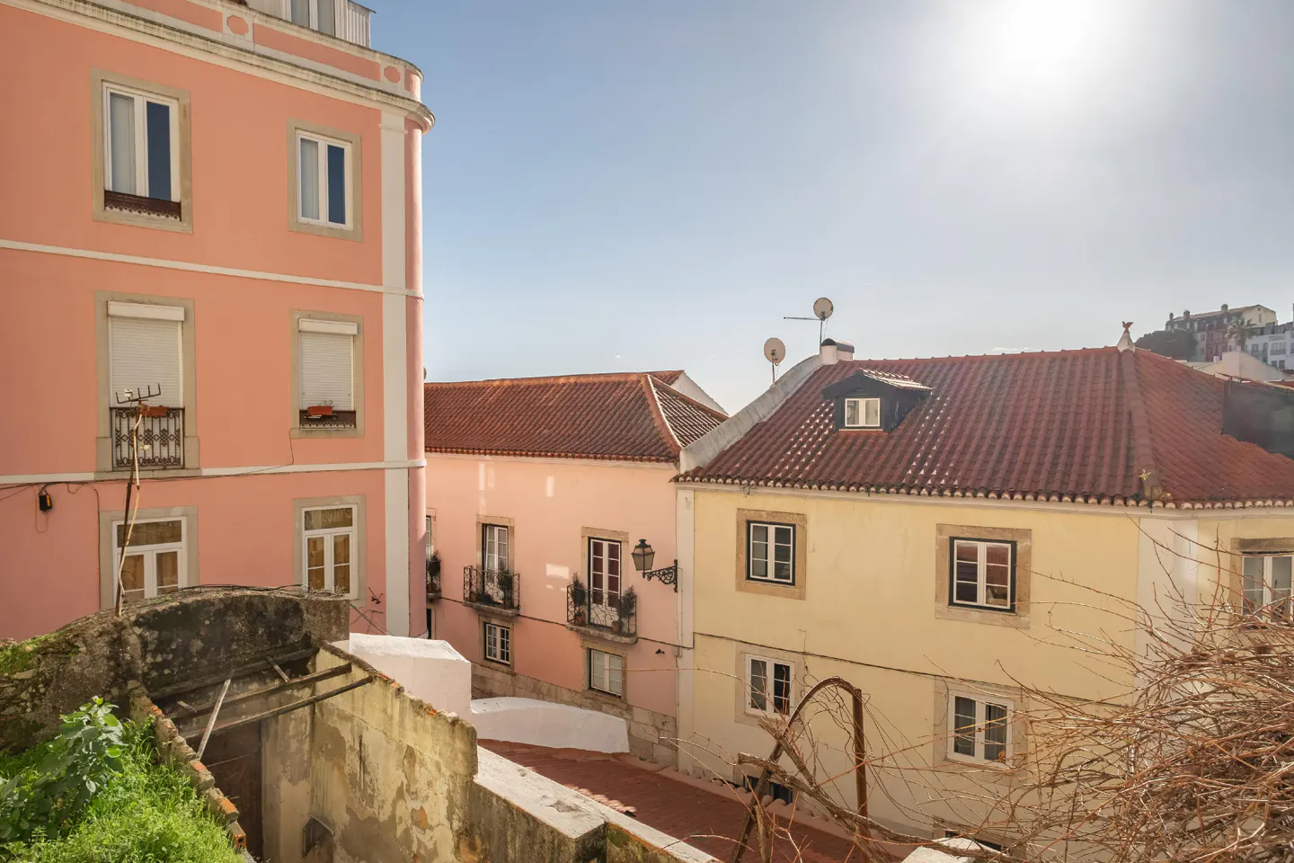 View of pastel buildings with red tile roofs under a bright blue sky in Lisbon, Portugal.