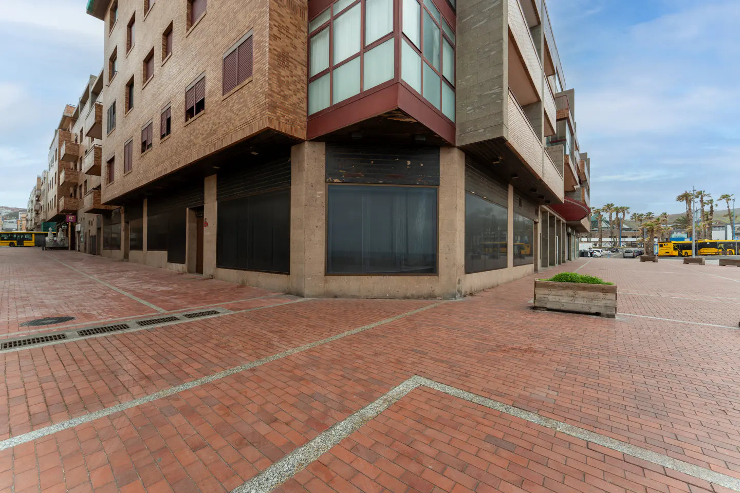 Exterior view of a multi-story building with brick facade and boarded-up storefronts on a brick-paved street.