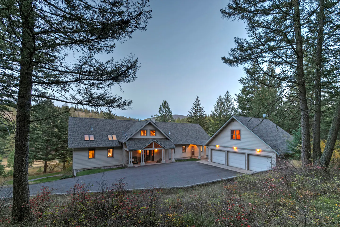 Exterior view of a tan house with a gray roof and a three-car garage, framed by trees.