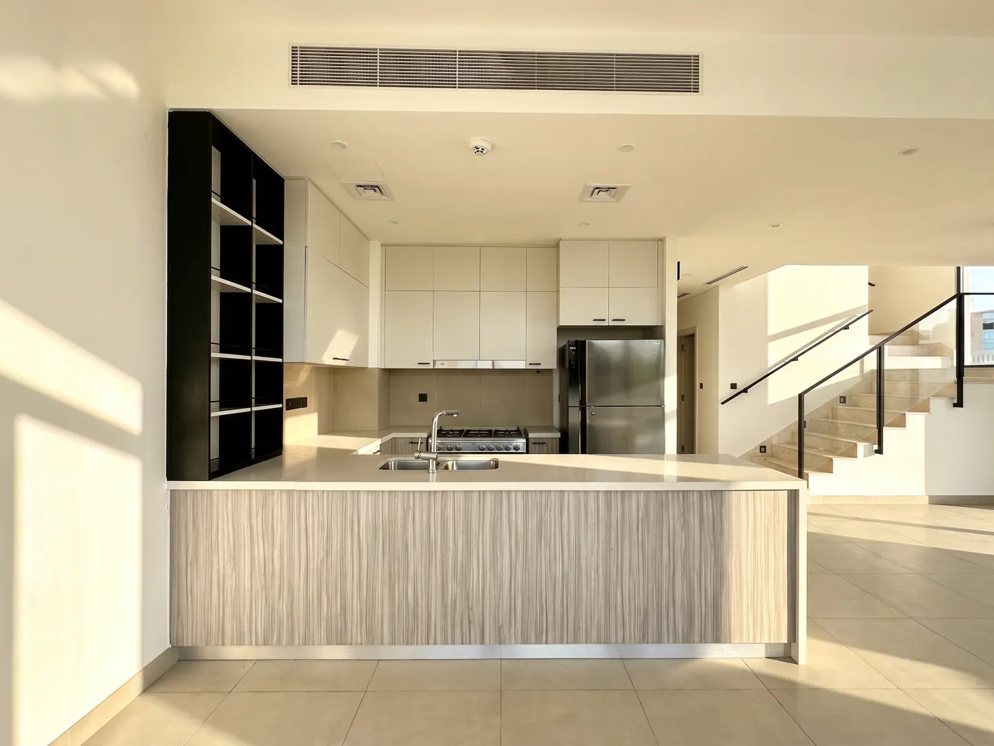 Bright, modern kitchen with white cabinets, stainless steel appliances, and a wood-paneled island. Stairs are visible in the background.