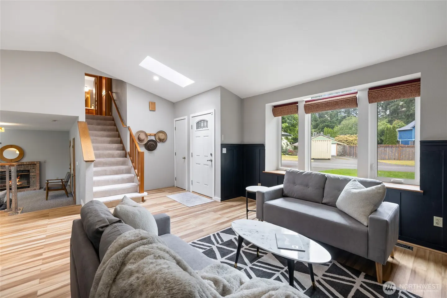 Bright living room with light wood floors, gray sofas, a marble coffee table, and stairs leading to an upper level.
