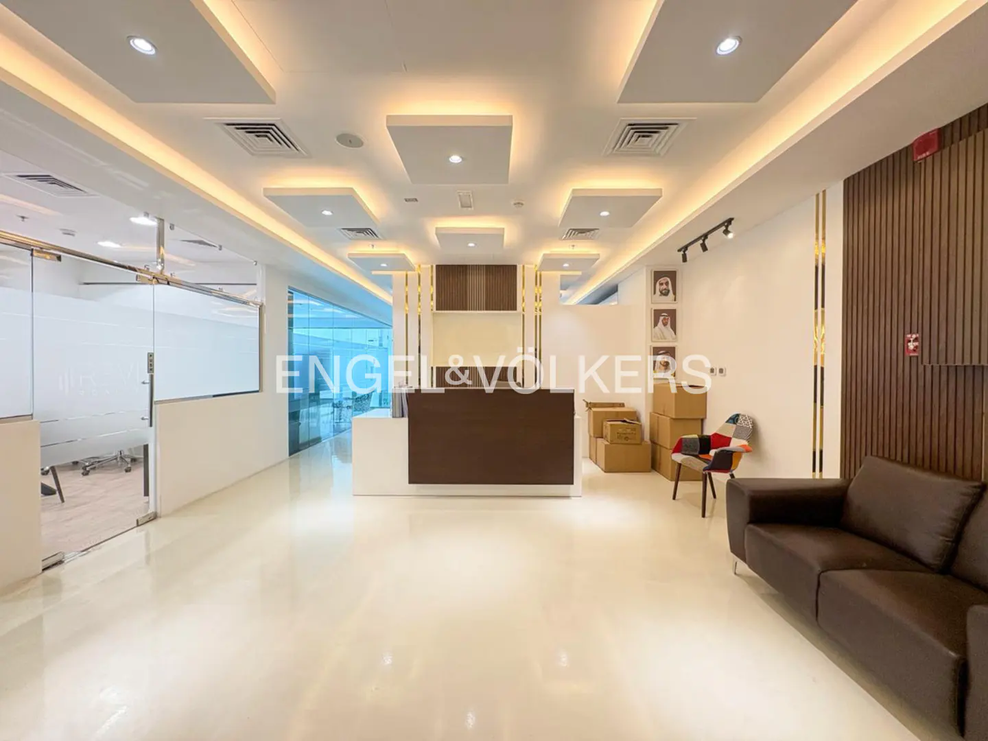 Office lobby with a brown reception desk, brown leather sofa, and boxes. The floor is white and shiny.