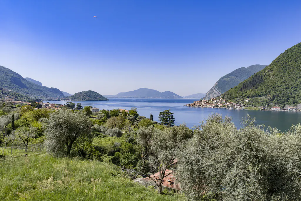 Scenic view of Lake Iseo, Italy, with green hills, blue water, and a small island village under a clear blue sky.