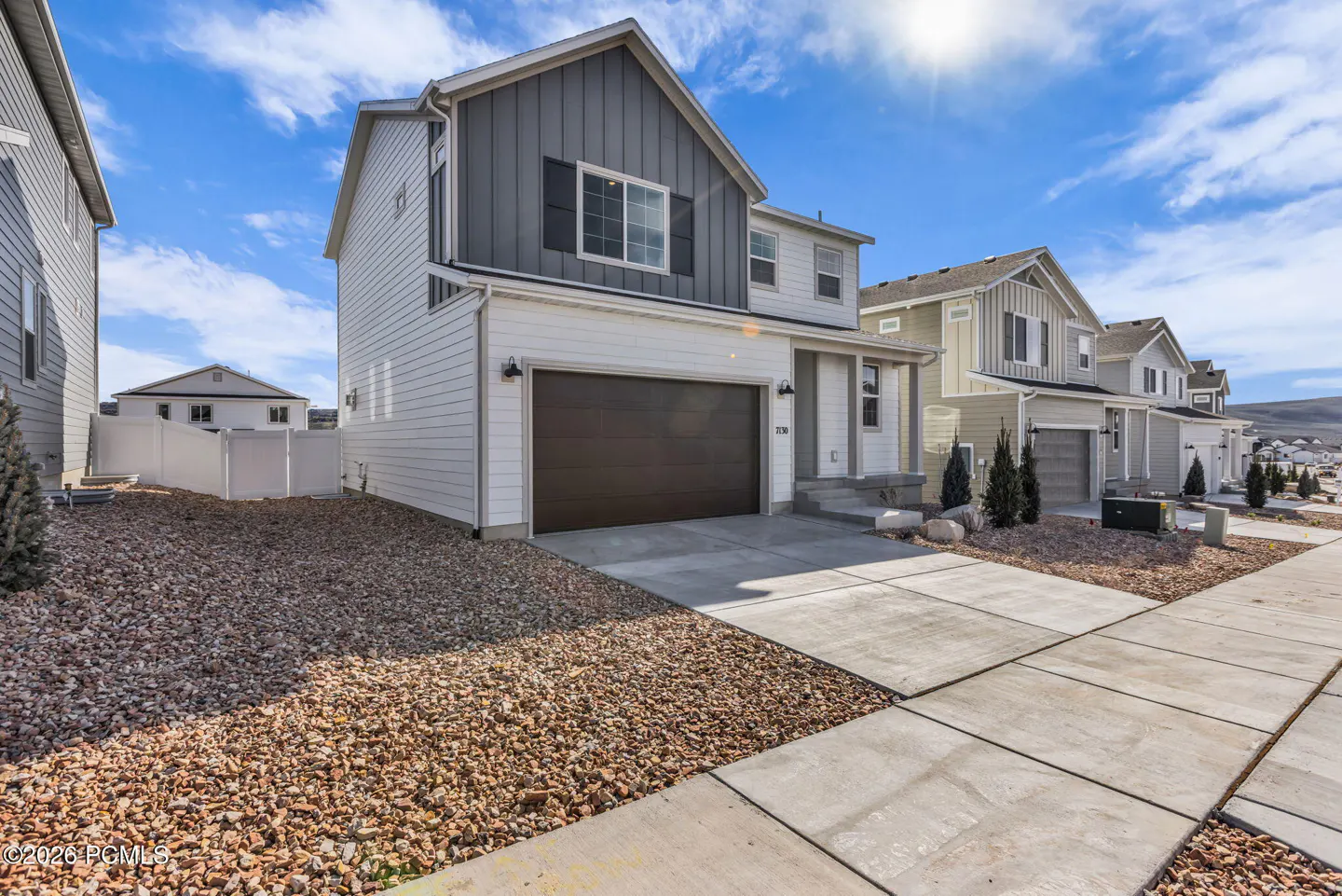 A two-story house with white siding, a gray gable, and a brown garage door on a sunny day.