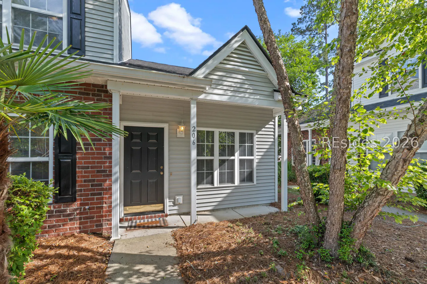 Exterior view of a two-story townhouse with gray siding, a black front door, and a small porch. A palm tree is on the left.