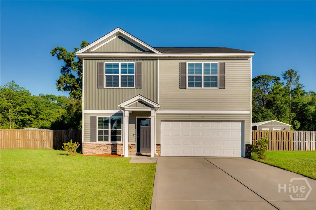 Two-story house with green siding, gray shutters, and a white garage door on a sunny day. A green lawn and blue sky are visible.