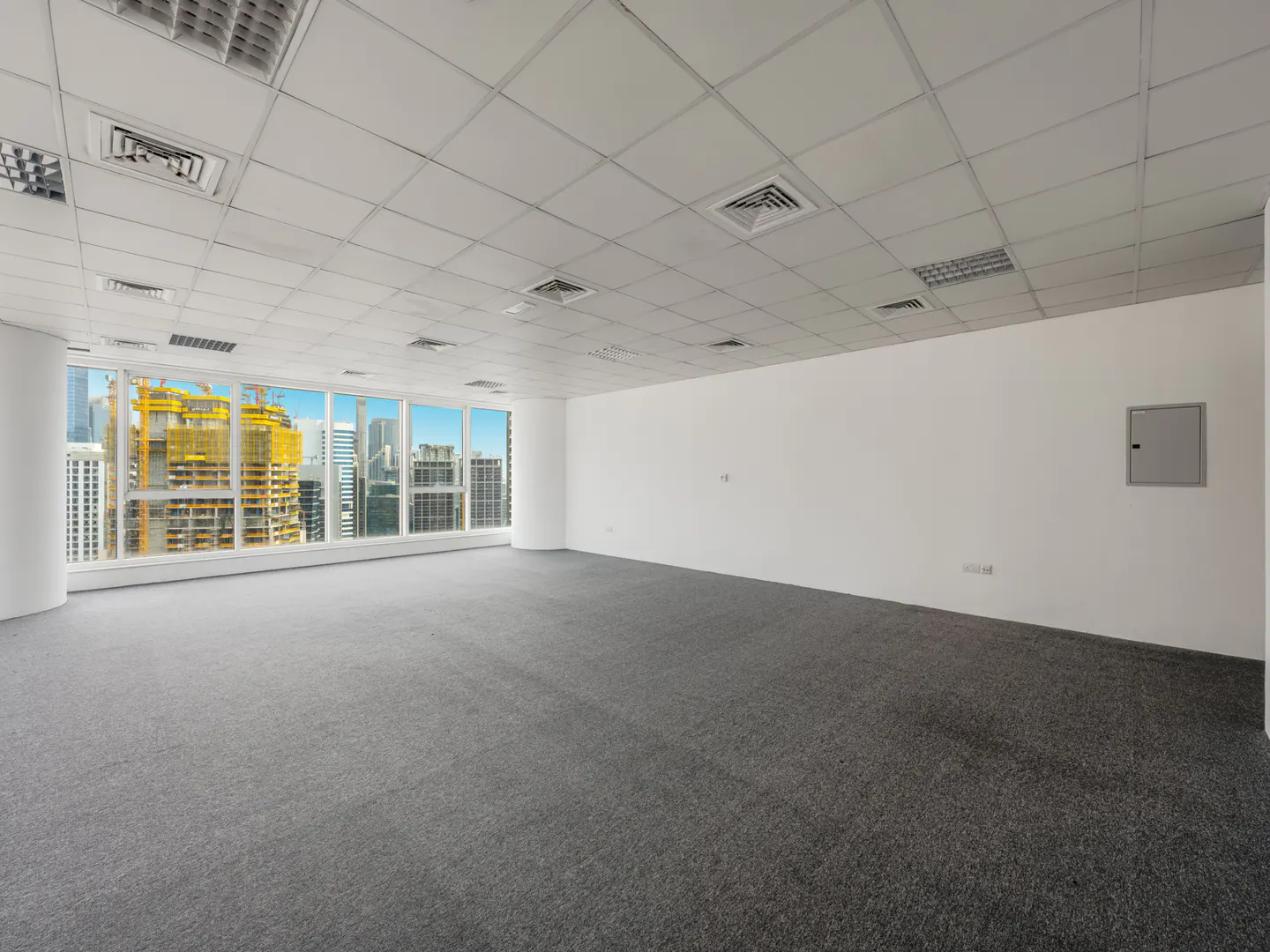 Empty office space with gray carpet, white walls, and a large window showing a city skyline with construction.