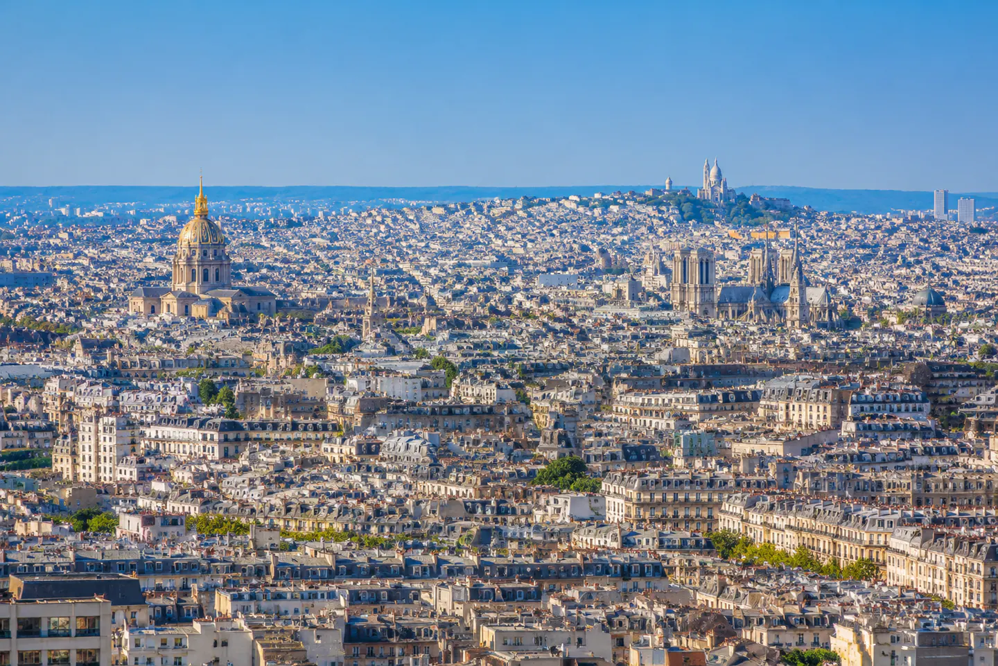 Paris cityscape under a clear blue sky. Landmarks include the golden dome of Les Invalides and Notre Dame Cathedral.