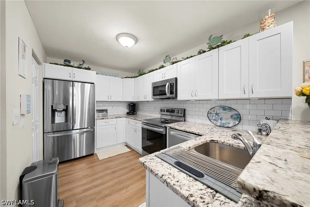 Bright kitchen with white cabinets, stainless steel appliances, and granite countertops. Coastal decor accents the space.